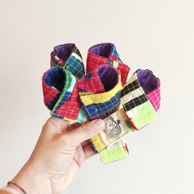 Laços de tecido coloridos com padrões de quadrados e etiqueta, segurados por mão.