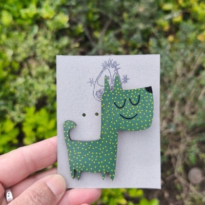 Figura de madeira em forma de cão verde com pontos amarelos e cartão cinzento com desenho de rosto