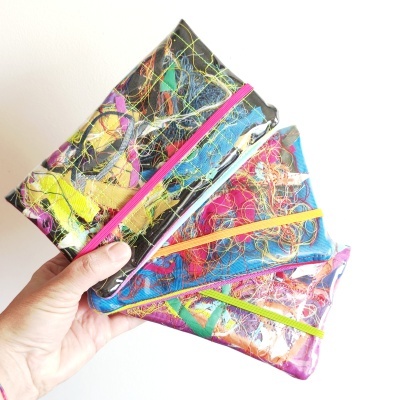 Três bolsas coloridas retangulares com camada plástica e elásticos coloridos