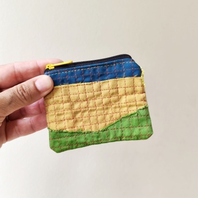 Carteira pequena acolchoada azul, amarelo e verde com fecho amarelo em fundo neutro