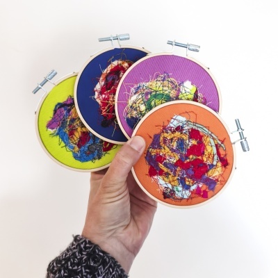 Quatro bastidores coloridos de bordado abstrato segurados por uma mão