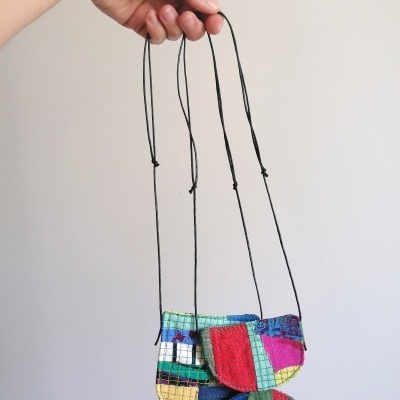 Três pequenas bolsas coloridas penduradas em cordão fino preto