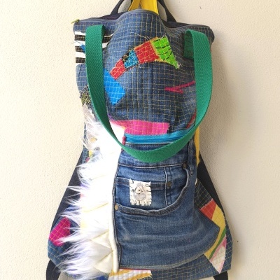 Mochila colorida de tecido com bolso jeans, detalhes de retalhos coloridos e franjas brancas.