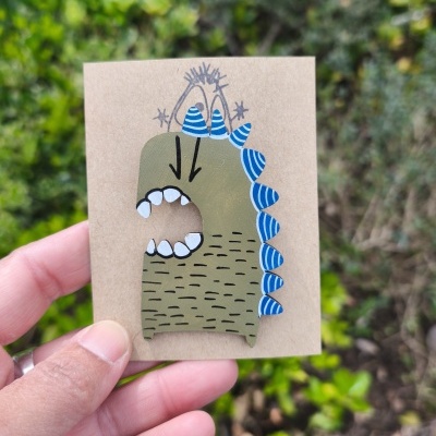 Anel de madeira pintado à mão com design de dinossauro verde e espinhos azuis