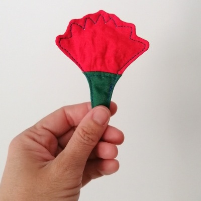 Flor vermelha e verde de tecido segurada por mão