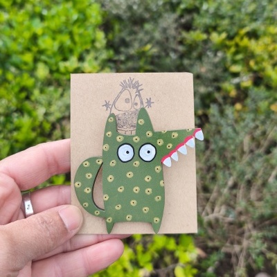 Broche verde com pontos amarelos e dentes brancos em cartão castanho claro