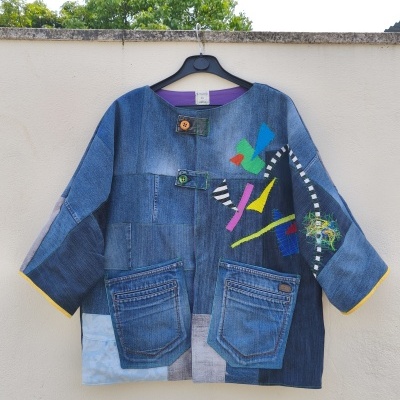 Casaco de ganga patchwork azul com aplicações coloridas pendurado na parede branca