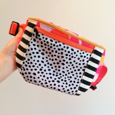 Bolsa carteira colorida com padrão de bolinhas pretas e riscas, fecho zip laranja e alça rosa