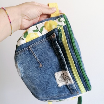 Mochila pequena em tecido jeans azul com interior estampado de limões e fechos verdes e amarelos
