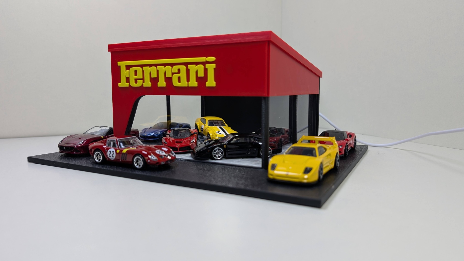 Miniaturas de carros Ferrari exibidas numa base de exposição com estrutura vermelha e logo amarelo Ferrari