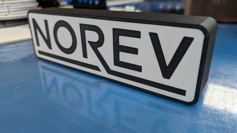 Placa rectangular branca com texto preto NOREV sobre superfície azul