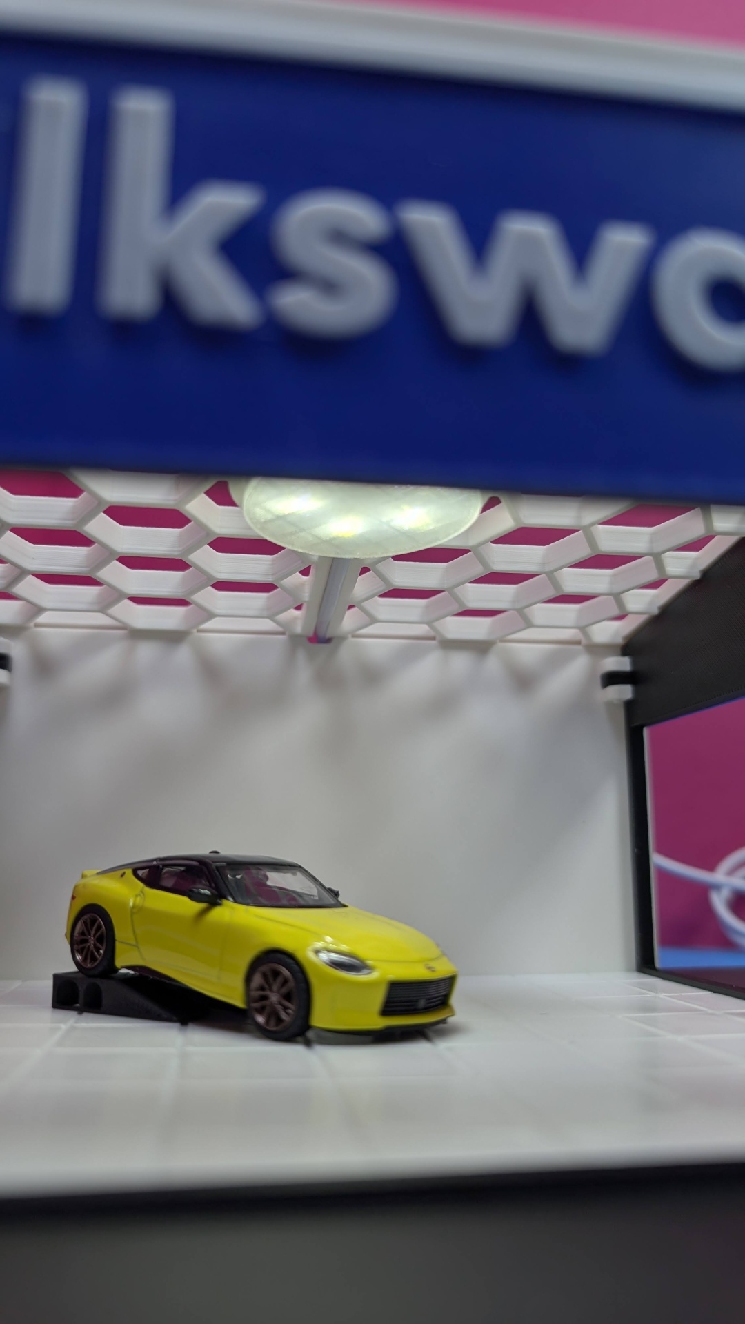 Miniatura de carro desportivo amarelo com tejadilho preto em suporte preto num cenário branco