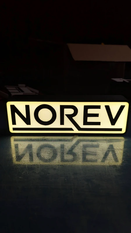 Placa luminosa rectangular com texto NOREV em branco e preto