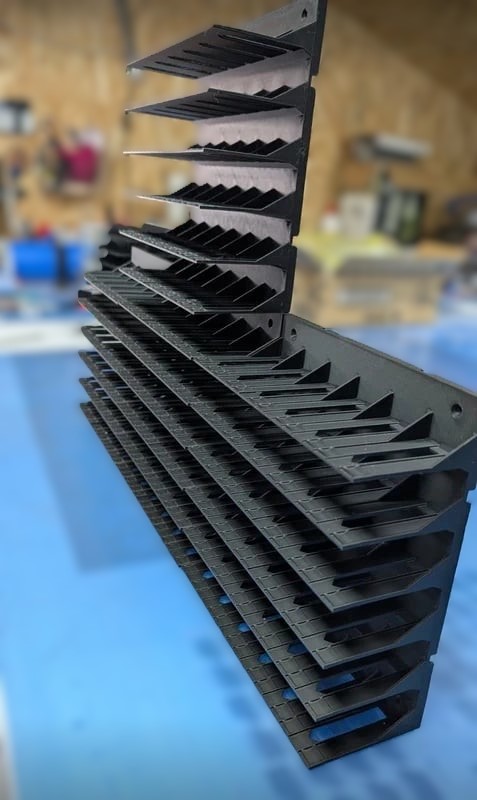 Estrutura metálica preta com prateleiras inclinadas e divisórias em V, suspensa em oficina