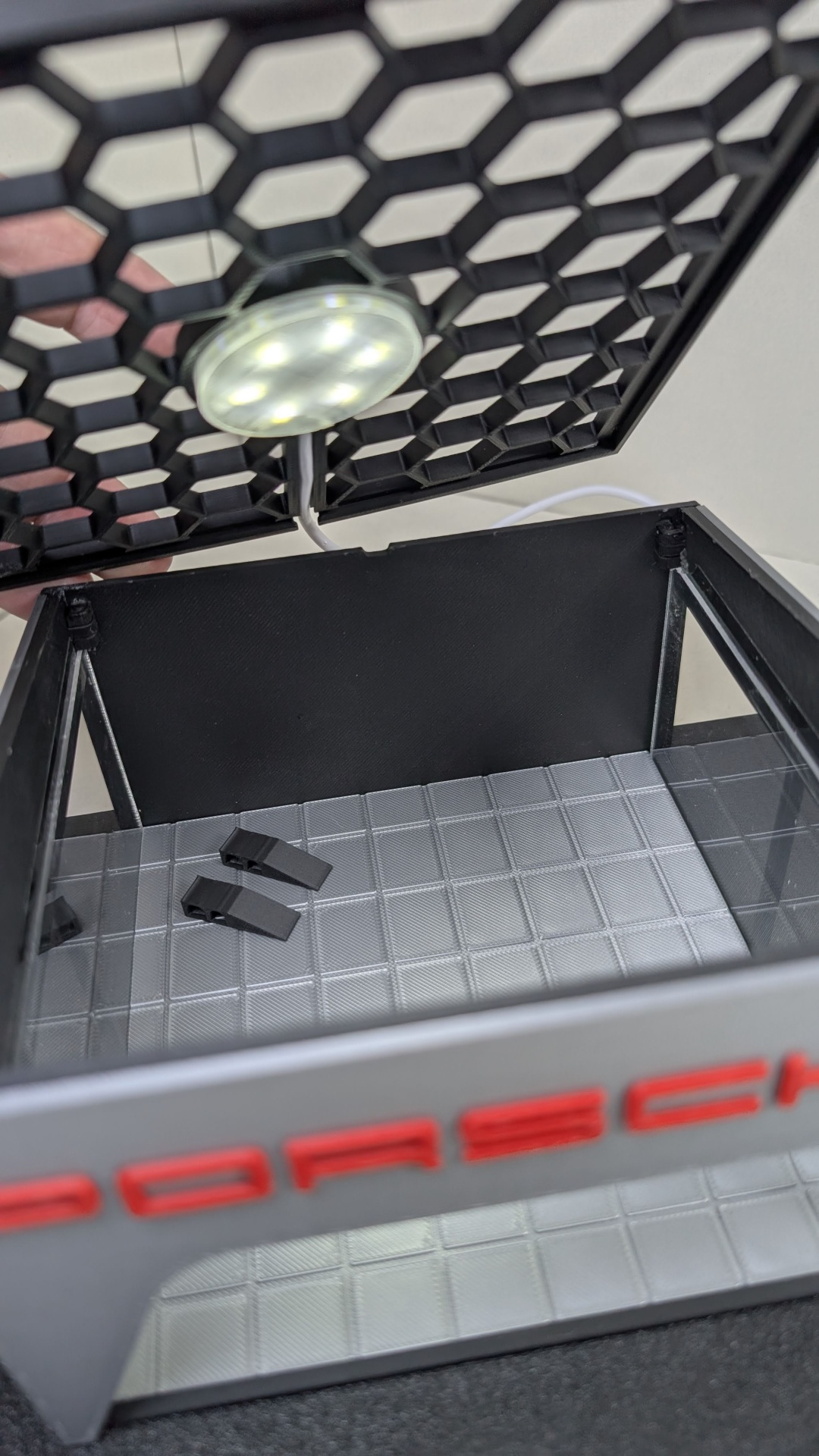 Caixa preta aberta com luz LED e texto PORSCHE vermelho na frente