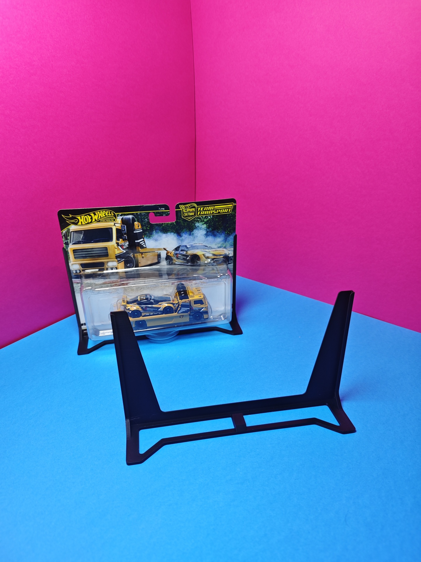 Miniatura Hot Wheels amarela e azul em embalagem com suporte preto