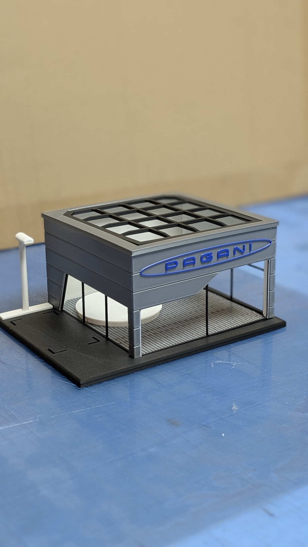 Maquete de edifício cinzento com janelas de vidro e placa azul com texto PAGANI