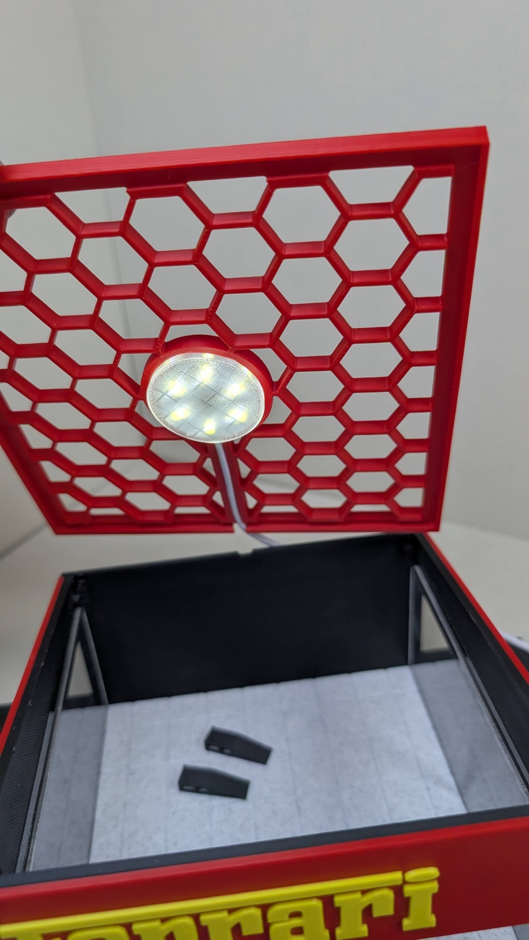 Caixa vermelha com grelha hexagonal, luz LED e interior claro com objetos pretos
