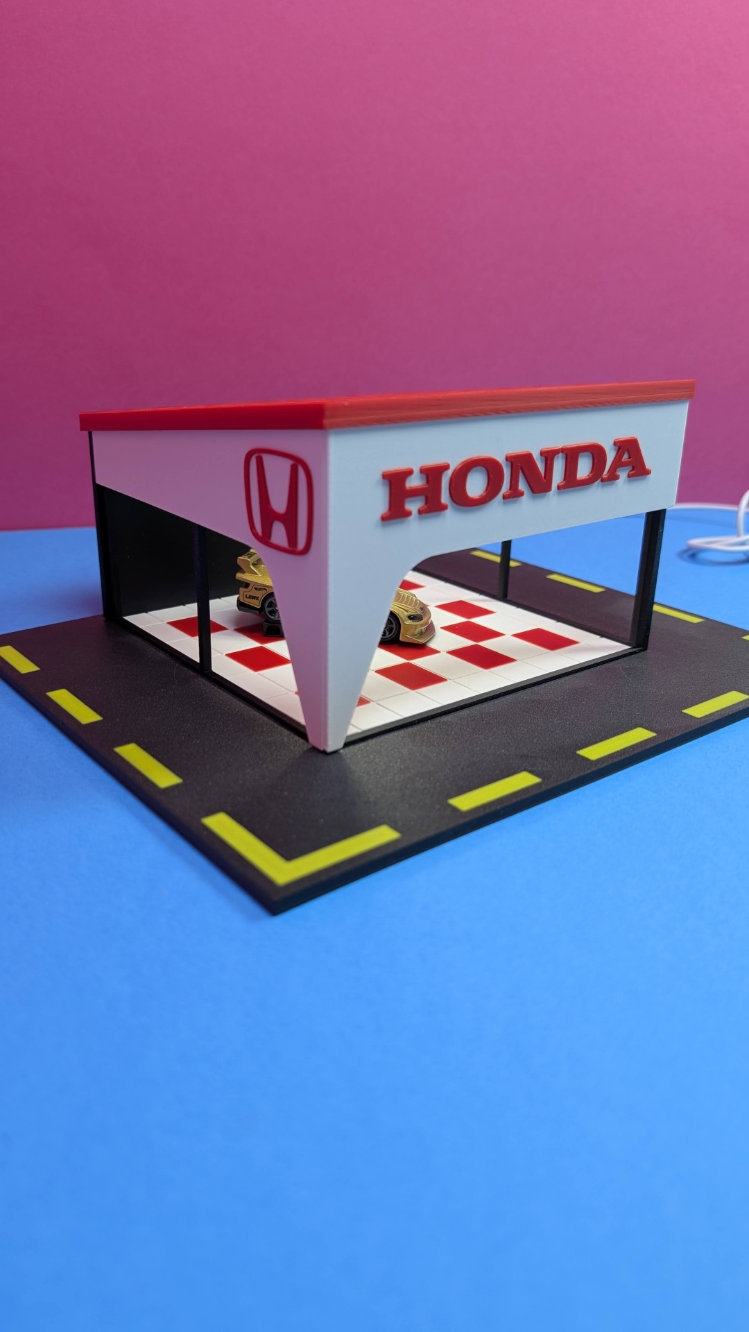 Miniatura de garagem Honda com carro dourado e chão xadrez