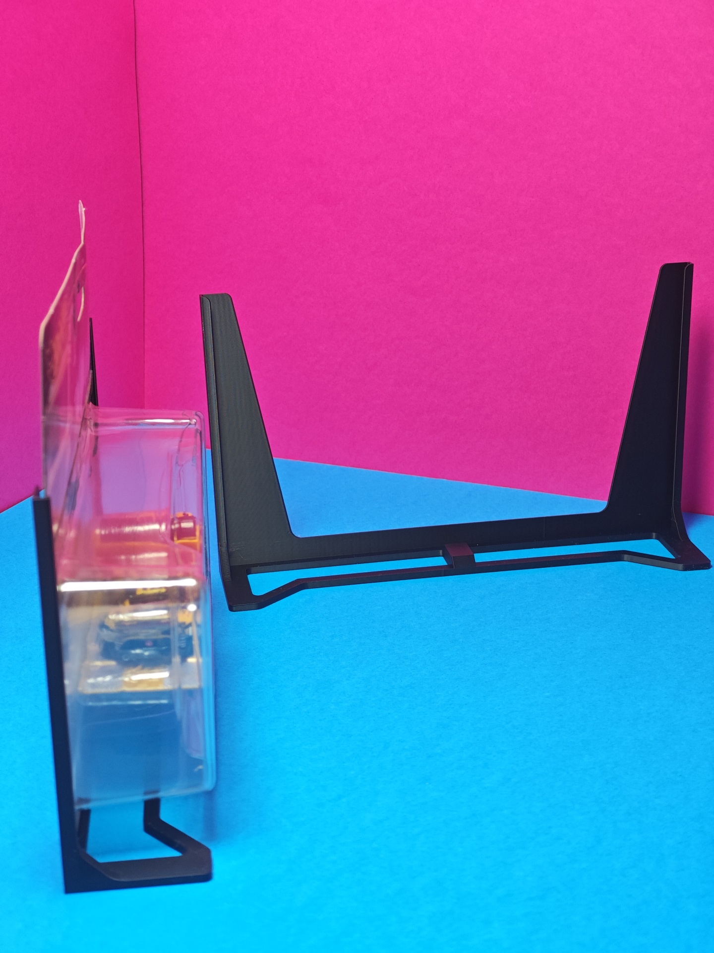 Suporte preto para consola ou equipamento eletrónico em fundo azul e rosa