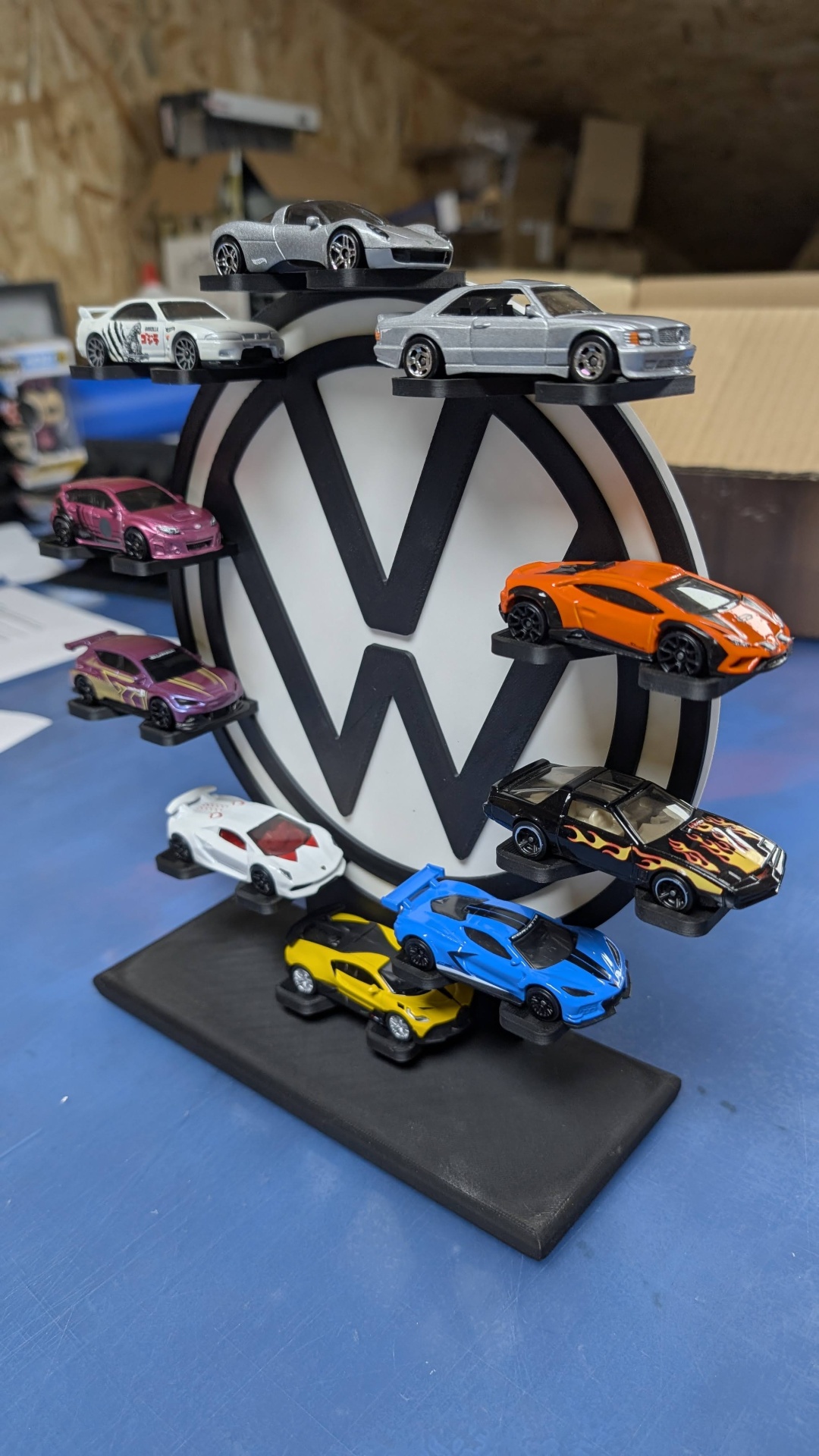 Expositor redondo com 10 miniaturas de carros coloridos em prateleiras ao redor de um logo preto e branco.