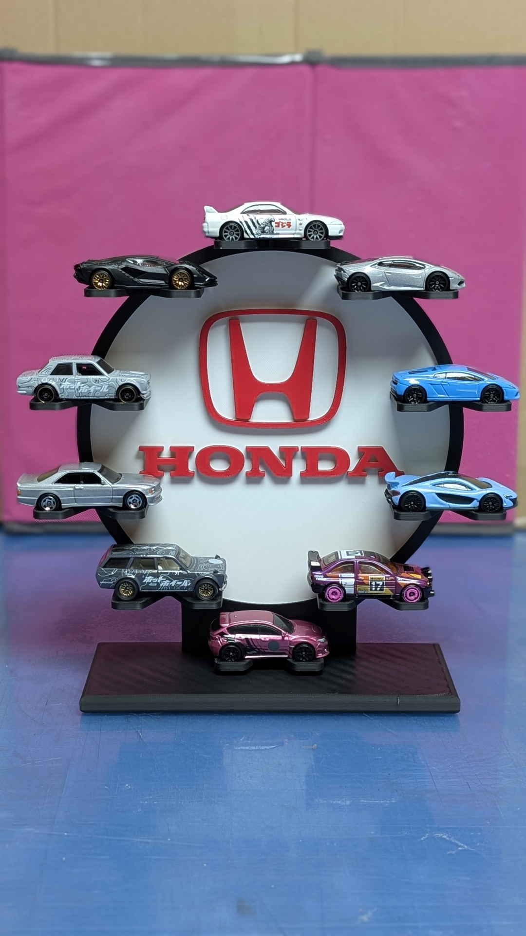 Expositor preto com miniaturas de carros e logótipo Honda vermelho no centro