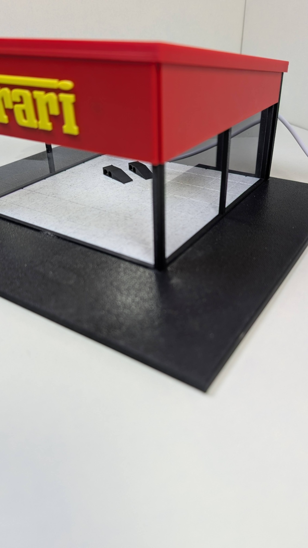 Miniatura de vitrina Ferrari vermelha e preta com painéis transparentes.