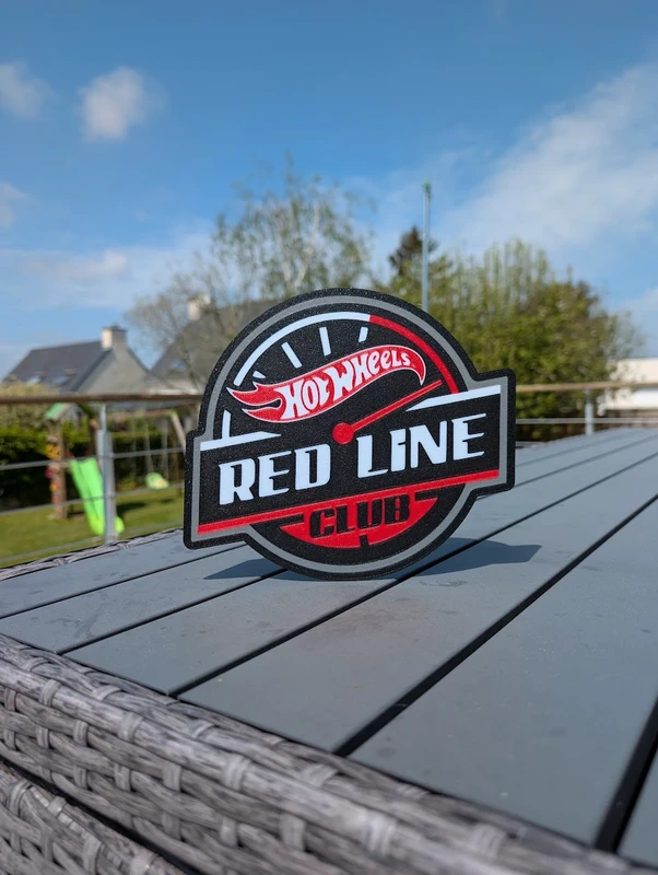 Emblema HOT WHEELS RED LINE CLUB em mesa cinza exterior com fundo de jardim