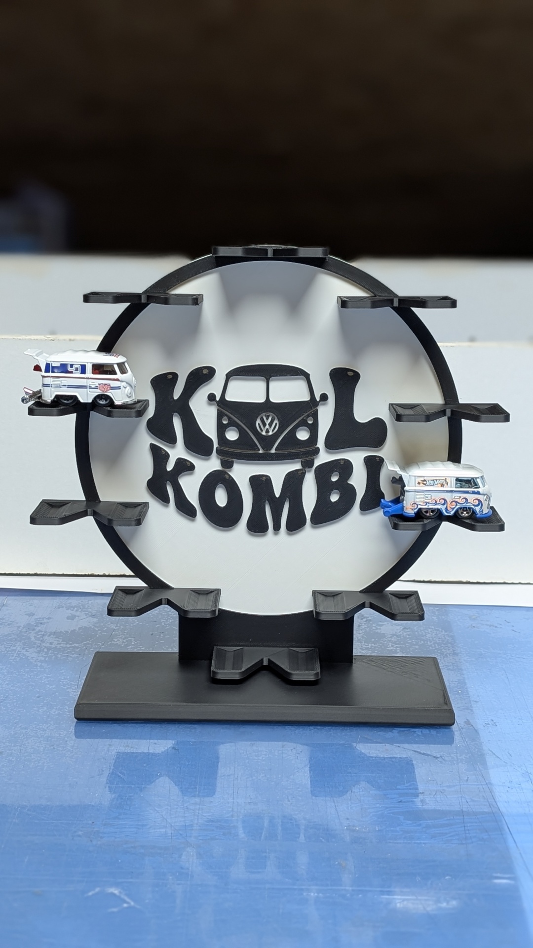 Expositor preto circular para carrinhos, com texto KOL KOMBI e desenho de carrinha VW Kombi.