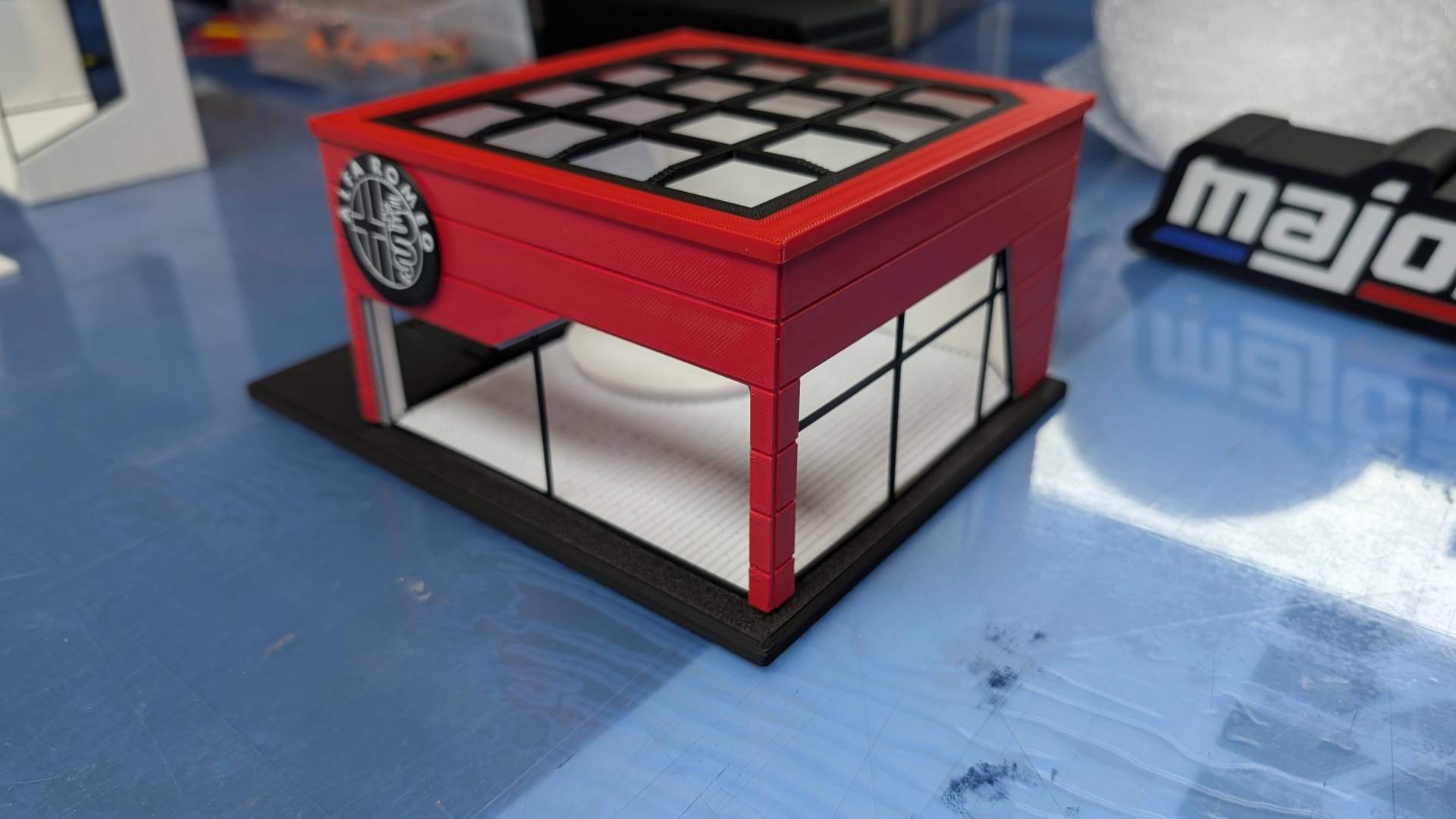 Maquete de edifício comercial vermelho com janelas transparentes e logótipo Alfa Romeo
