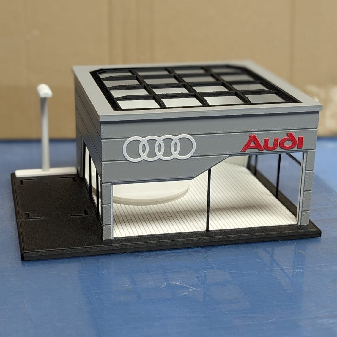 Modelo 3D pequeno de edifício Audi cinzento com teto branco e logo vermelho e branco