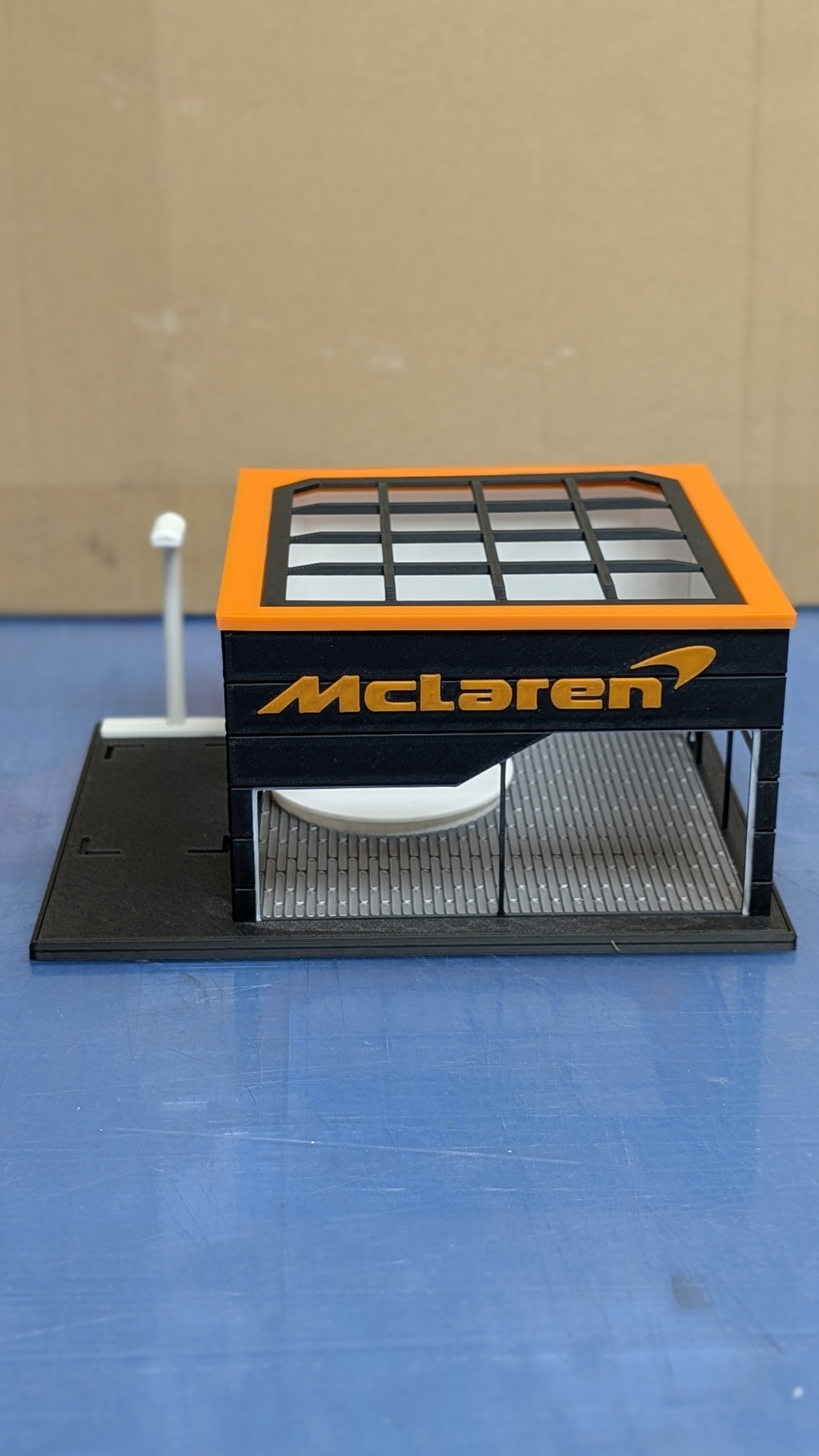 Miniatura de quiosque McLaren preto e laranja com janelas de vidro