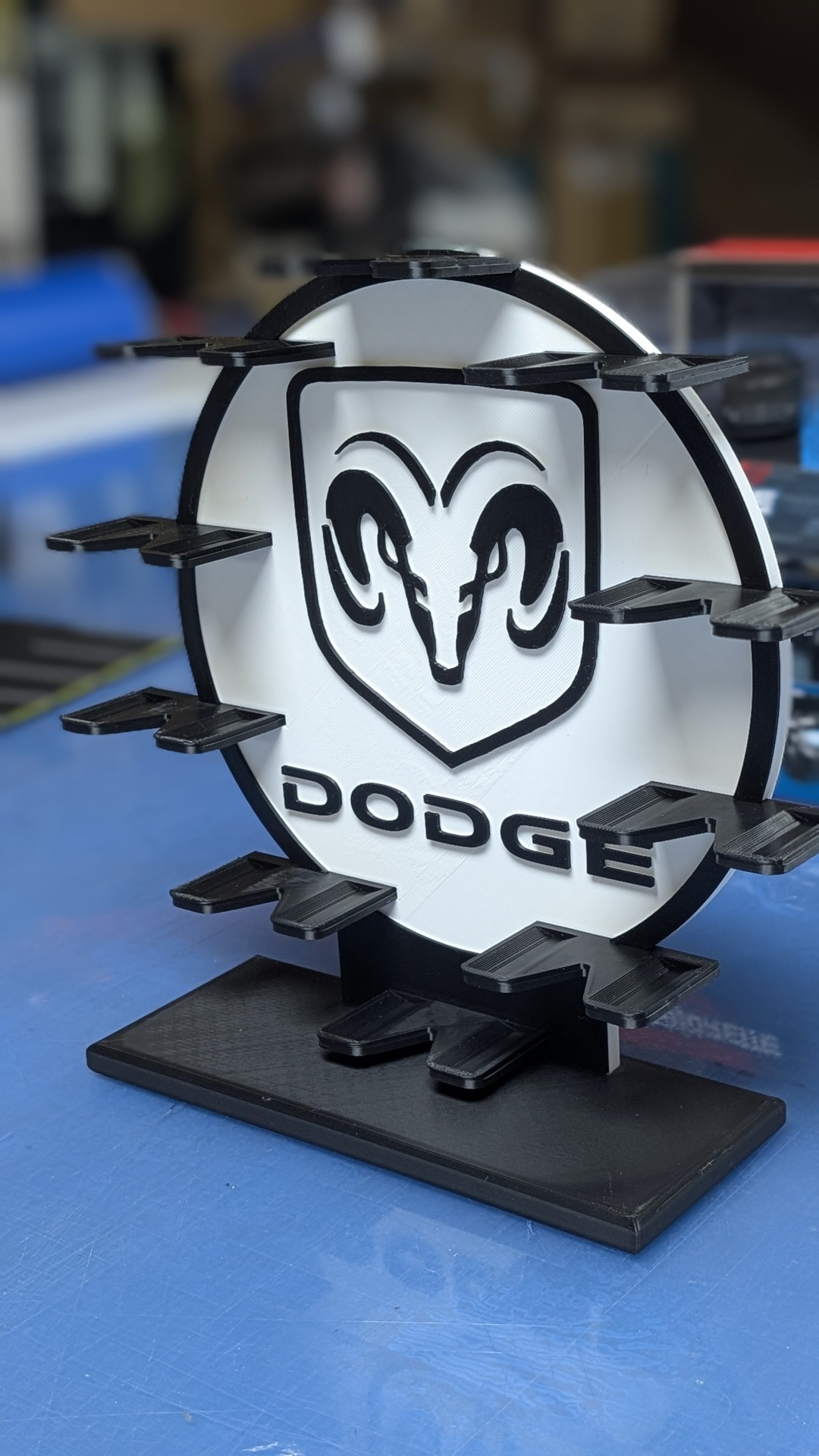 Suporte em plástico preto e branco com logótipo Dodge e presilhas em mesa azul.