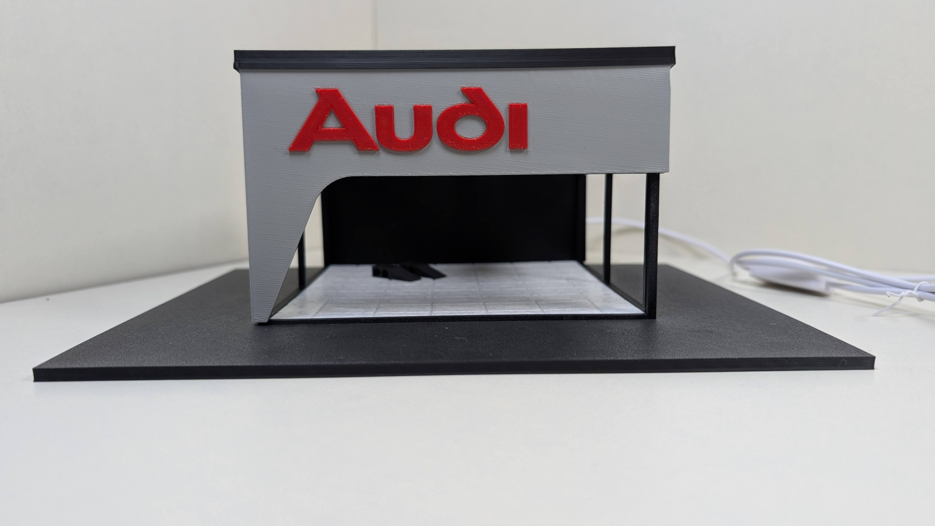 Miniatura de um stand Audi cinza e preto com logotipo vermelho