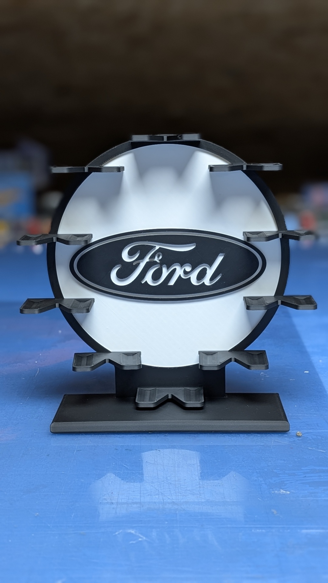 Suporte de exposição com logo Ford em branco e preto sobre base azul.