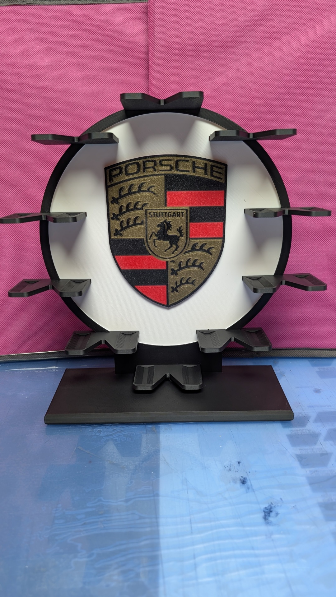 Suporte preto com logo Porsche em fundo branco e rosa.