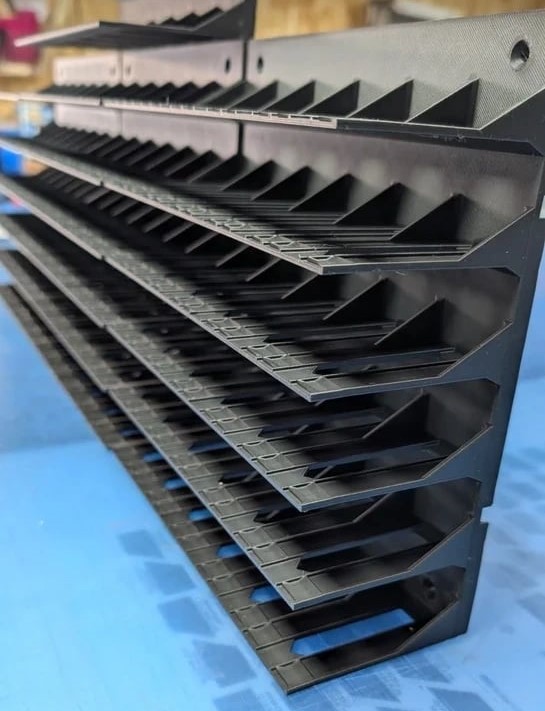 Estrutura preta de plástico com prateleiras inclinadas e divisórias sobre superfície azul