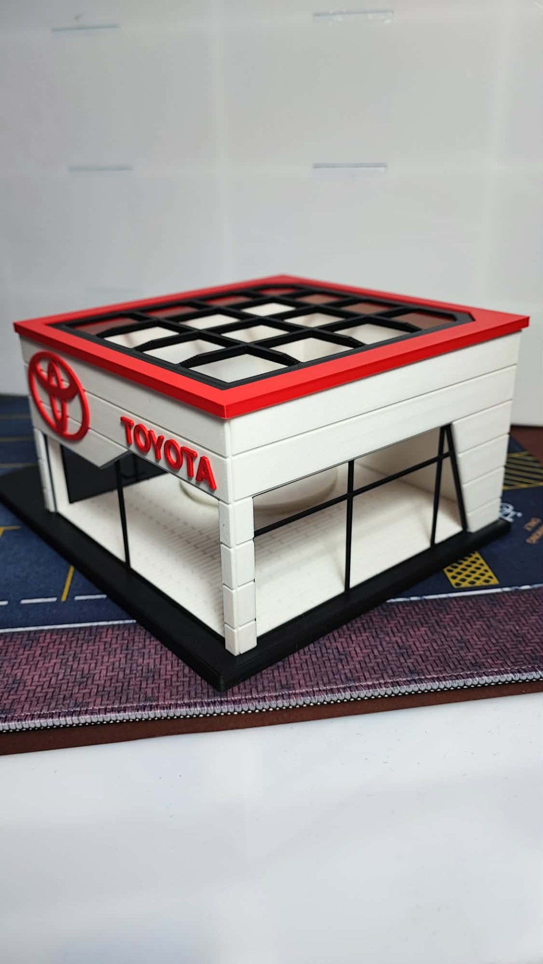 Miniatura de loja Toyota branca com detalhes vermelhos e pretos.
