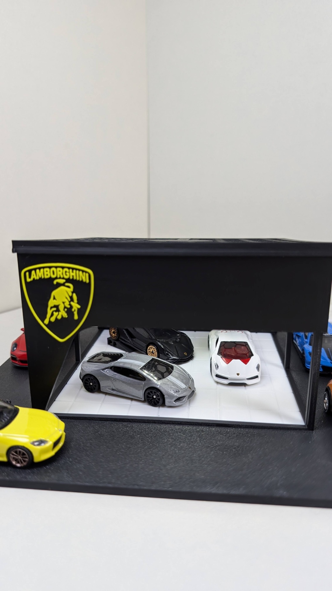 Miniaturas de carros de coleção numa garagem preta com o logo Lamborghini amarelo