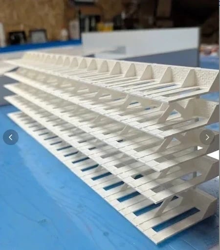 Estrutura branca com camadas horizontais e suportes triangulares sobre superfície azul