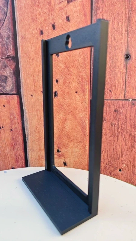 Suporte de metal preto vertical com base larga sobre mesa branca e fundo de parede imitando madeira.