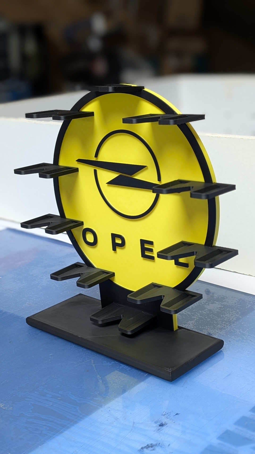 Expositor de mesa amarelo e preto com logótipo OPEL e suportes para pendurar objetos.