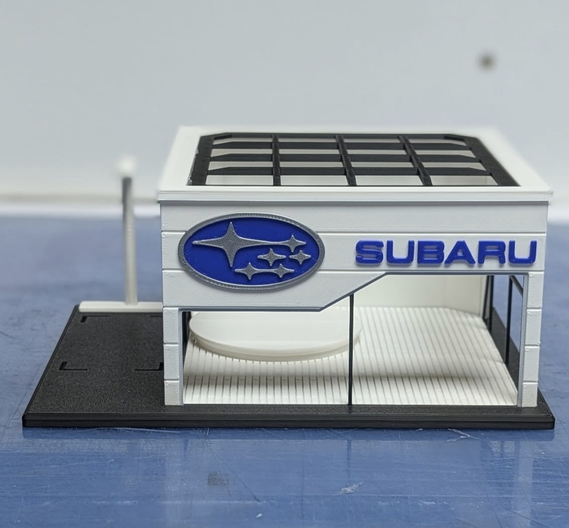 Miniatura de concessionária Subaru com logótipo e texto em azul.