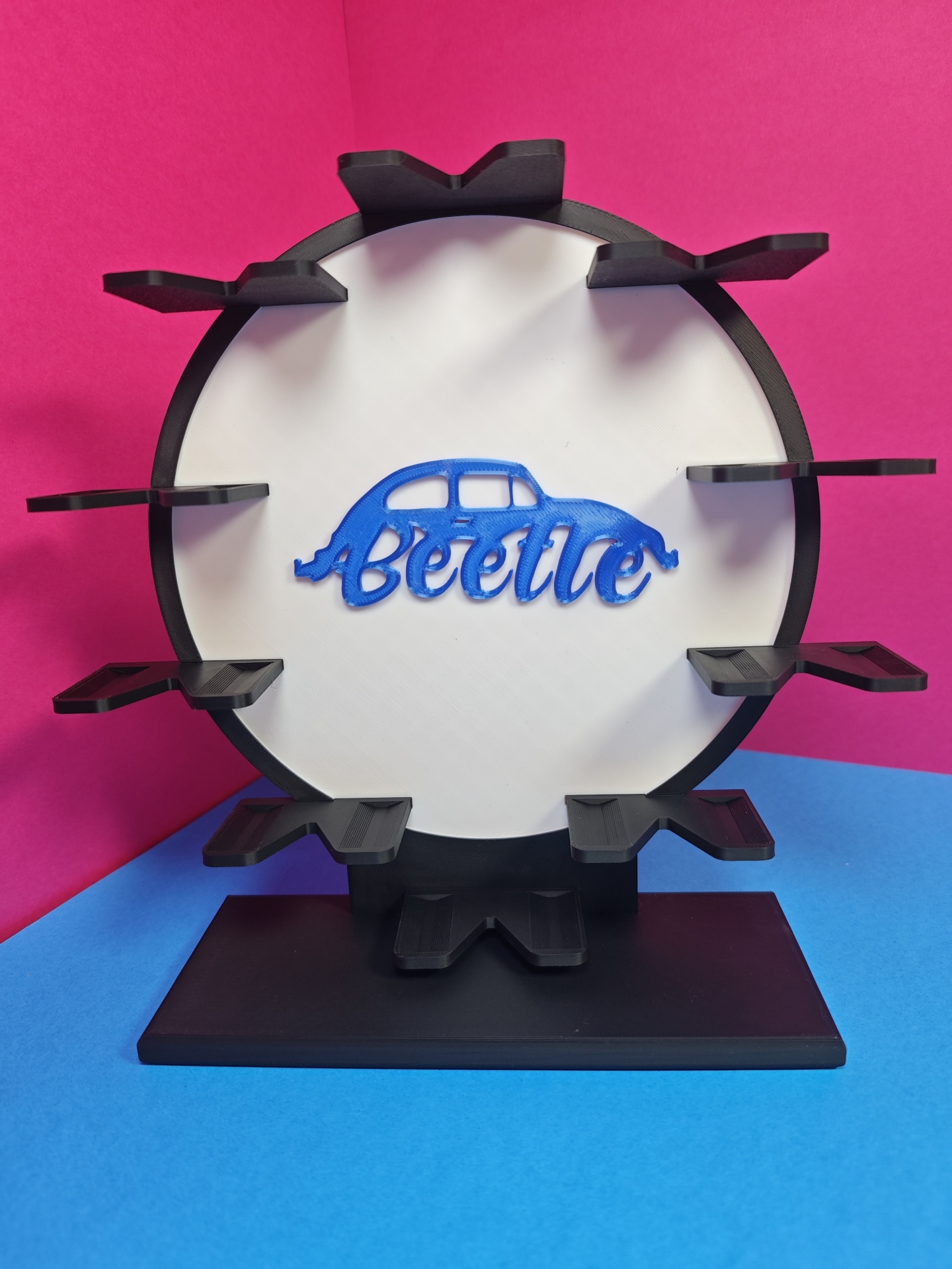 Estrutura redonda preta com painel branco e suporte para objetos, com texto Beetle azul e desenho de carrinha Beetle.