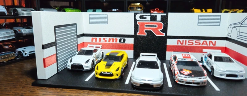 Miniaturas de carros Nissan GT-R em exposição temática com parede e chão em cenário de garagem.