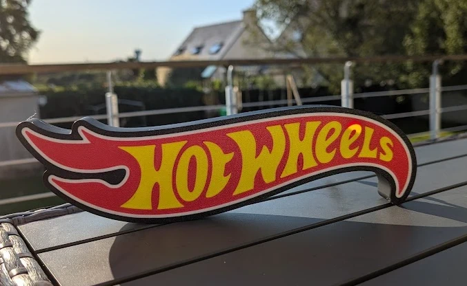 Placa decorativa HOT WHEELS em plástico vermelho e amarelo numa mesa ao ar livre