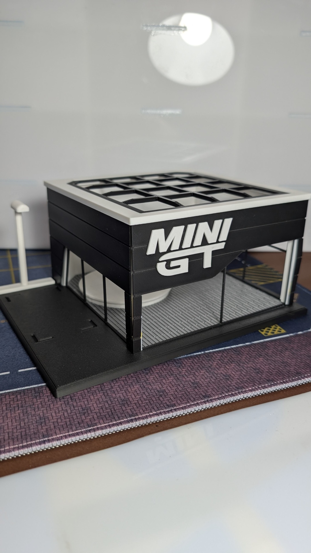 Miniatura preta de edifício com janelas transparentes e texto MINI GT na lateral.