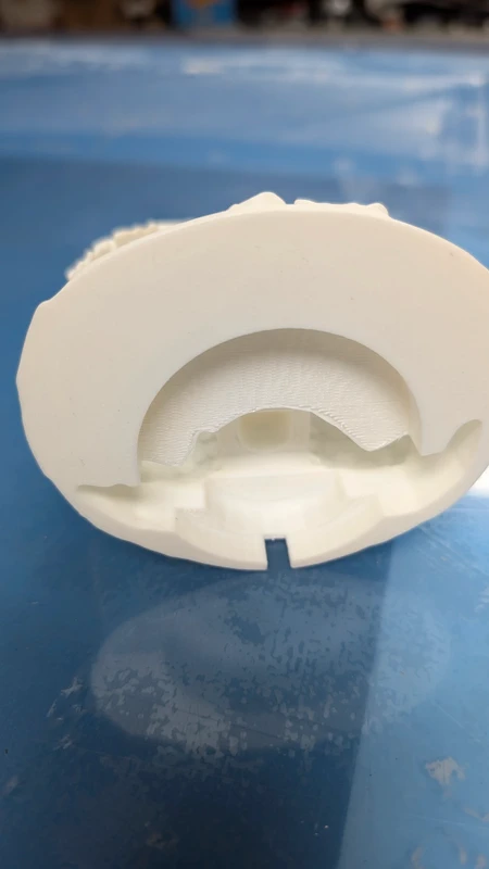 Peça plástica branca com recortes sobre superfície azul