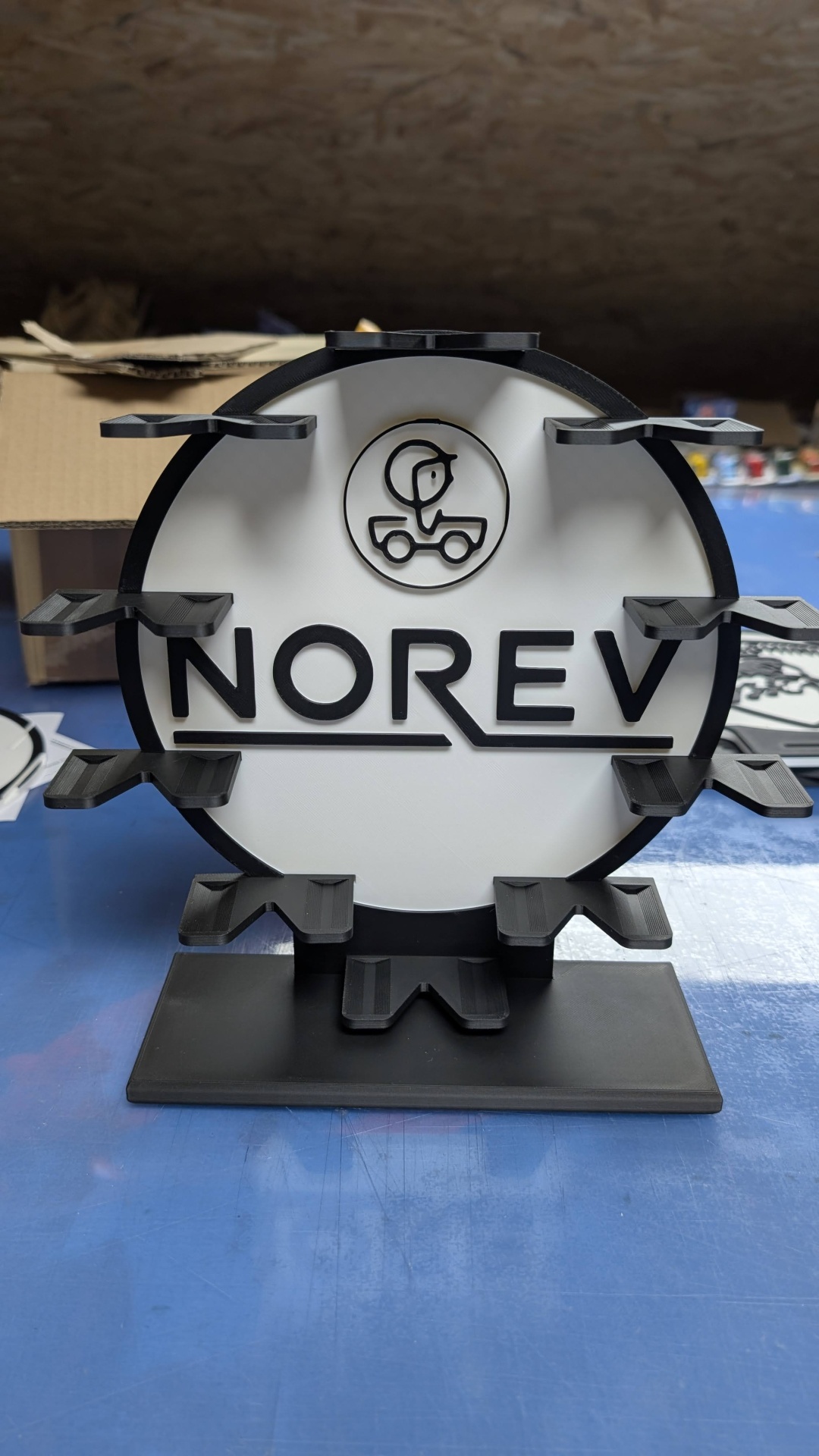 Suporte de exposição circular preto e branco com texto NOREV e plataformas para objetos