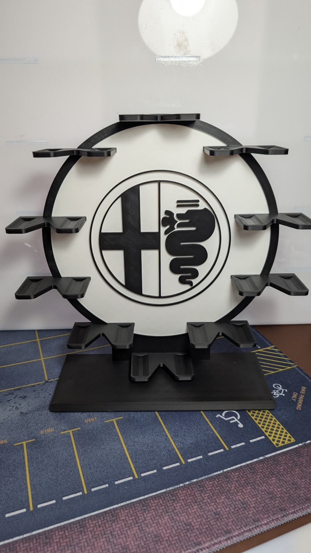 Suporte de mesa preto e branco com símbolo e várias prateleiras em cima de tapete com marcações de estacionamento